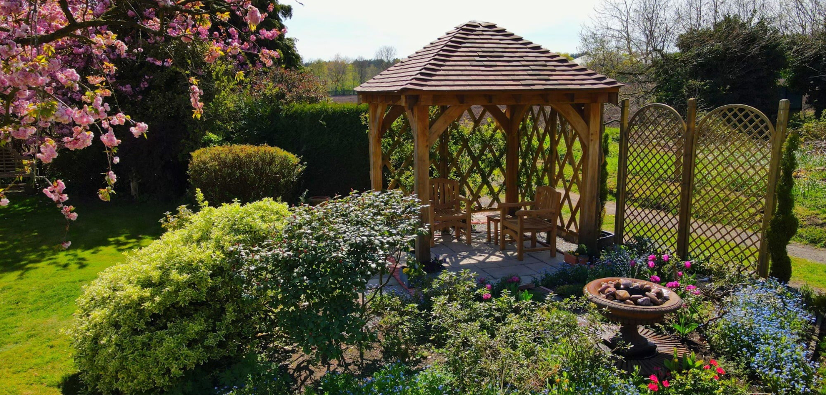 Oak gazebo situated in a garden with conifers.